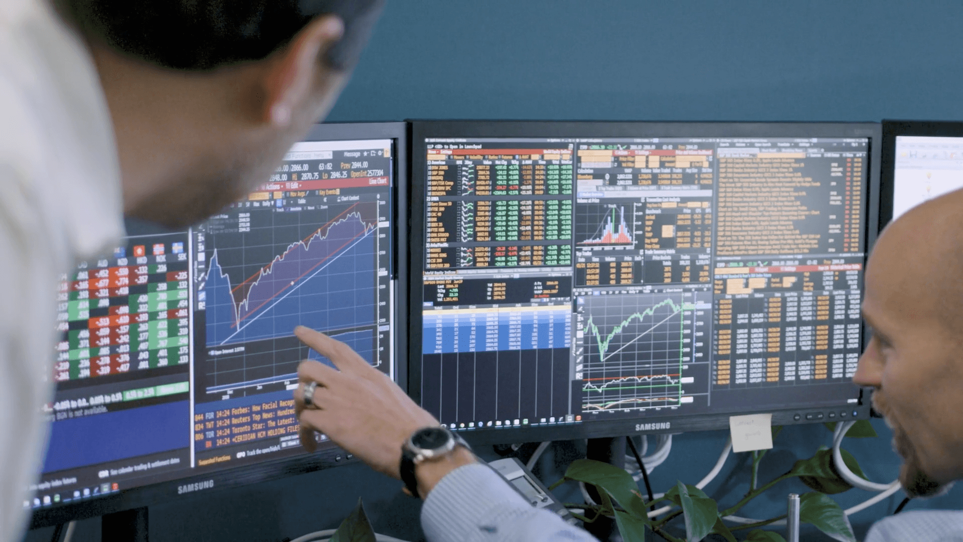 Two people review financial data and stock charts related to PERA Investments on dual computer monitors displaying colorful graphs and tables in an office setting.