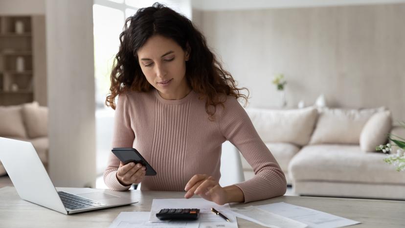 A woman sitting in front of a computer and using a calculator.