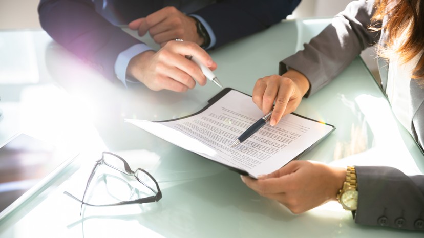 Two people in business attire are reviewing a document. Glasses are nearby.