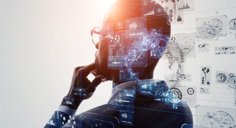 A person in a suit, viewed from behind, examines holographic digital interfaces filled with various data and graphs, suggesting deep thought and analysis.