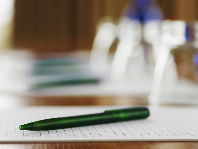 A close-up photo of a green pen laying on a paper pad, there are more blurred in the background.