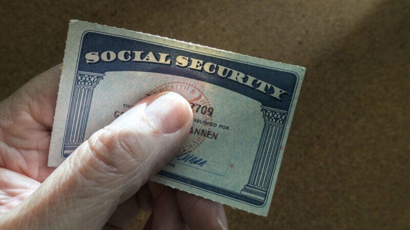 A hand holding a U.S. Social Security card displaying some visible text and numbers.