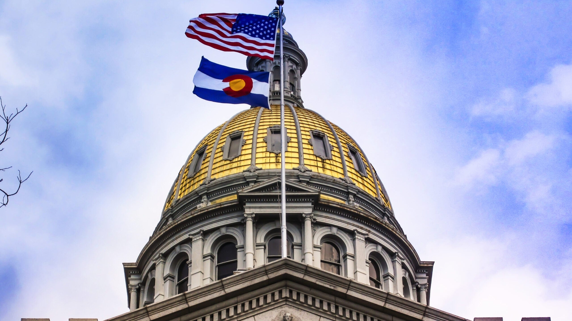 Golden Capitol Dome in Denver with the American flag and the Colorado flag blowing in the wind.